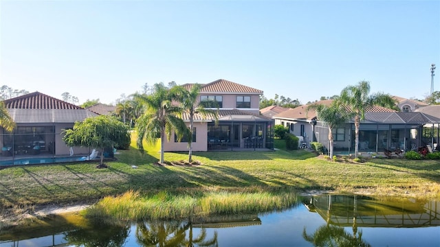 rear view of house with a water view, glass enclosure, and a lawn