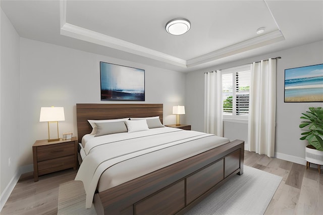 bedroom with light wood-type flooring, a raised ceiling, baseboards, and crown molding