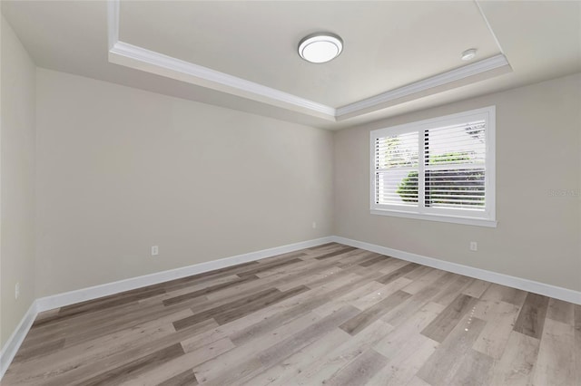 spare room with a tray ceiling, light wood-style flooring, crown molding, and baseboards