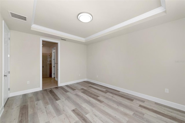 unfurnished room with visible vents, light wood-type flooring, a raised ceiling, and baseboards