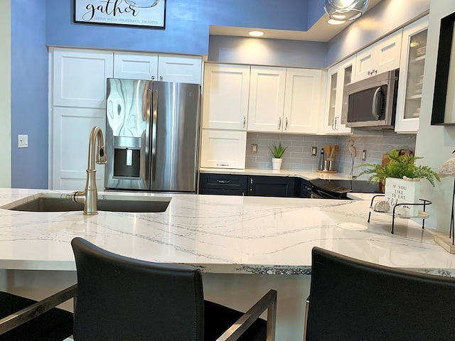 kitchen featuring stainless steel appliances, light stone countertops, sink, and white cabinets