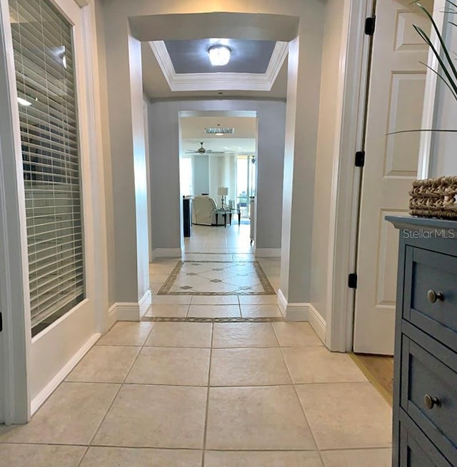 corridor with a raised ceiling, ornamental molding, and light tile patterned flooring