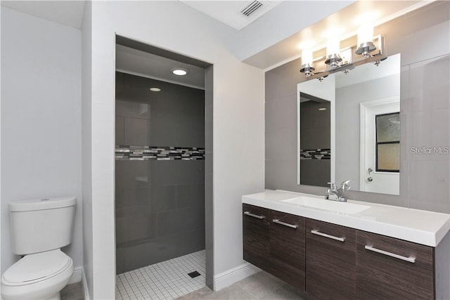 bathroom with tile patterned flooring, vanity, a tile shower, and toilet