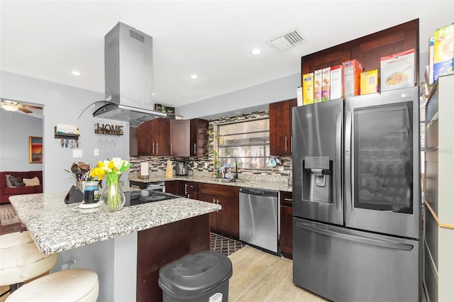 kitchen with appliances with stainless steel finishes, island range hood, sink, a breakfast bar area, and backsplash