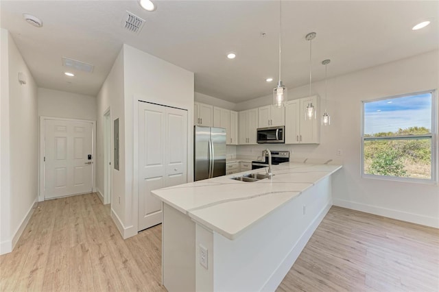 kitchen featuring decorative light fixtures, kitchen peninsula, stainless steel appliances, light hardwood / wood-style floors, and white cabinets