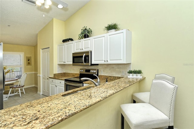 kitchen featuring white cabinetry, appliances with stainless steel finishes, light stone countertops, and vaulted ceiling