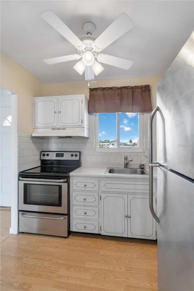 kitchen featuring appliances with stainless steel finishes, white cabinetry, sink, decorative backsplash, and light hardwood / wood-style floors