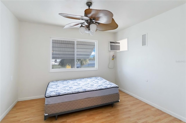 bedroom featuring ceiling fan, an AC wall unit, and light wood-type flooring