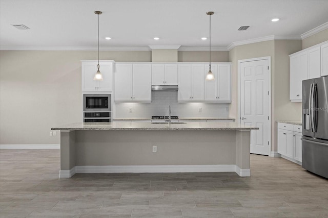 kitchen featuring appliances with stainless steel finishes, light stone countertops, white cabinets, a center island with sink, and decorative light fixtures