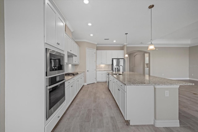 kitchen with light stone counters, decorative light fixtures, a center island with sink, stainless steel appliances, and white cabinets