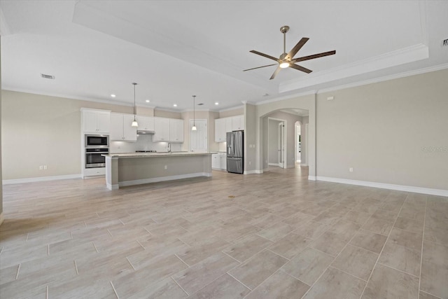 unfurnished living room featuring ceiling fan, ornamental molding, a tray ceiling, and light hardwood / wood-style floors