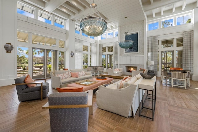 living room with beamed ceiling, a large fireplace, a chandelier, and french doors