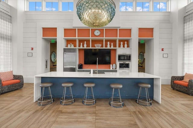 kitchen with built in appliances, light hardwood / wood-style flooring, a kitchen breakfast bar, and a high ceiling