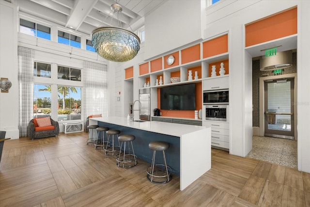 kitchen featuring a towering ceiling, a breakfast bar area, white cabinets, a notable chandelier, and beam ceiling