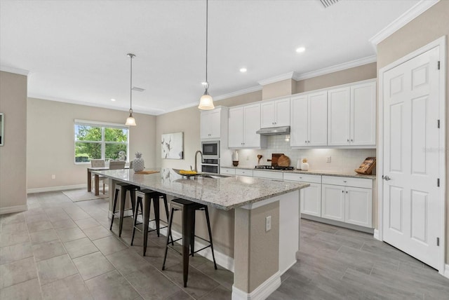 12029 Perennial Pl, Lakewood Ranch, FL 34211 - kitchen with a sink, under cabinet range hood, a center island with sink, stainless steel microwave, and white cabinetry