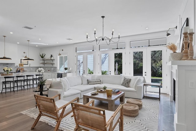 living area with a healthy amount of sunlight, light wood finished floors, a chandelier, and french doors