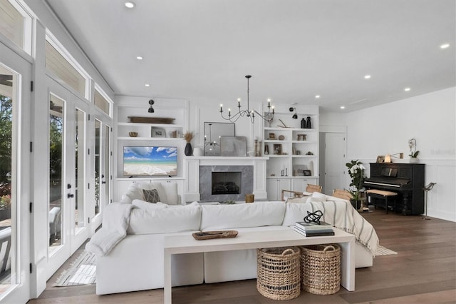 living area featuring a high end fireplace, dark wood-type flooring, an inviting chandelier, built in shelves, and recessed lighting