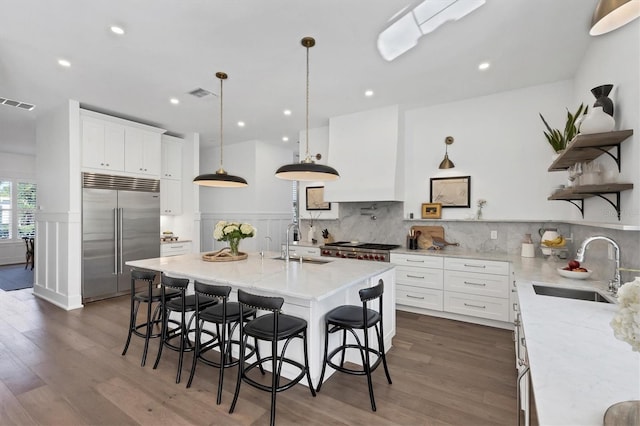 kitchen featuring premium range hood, a sink, white cabinets, stainless steel built in refrigerator, and decorative light fixtures