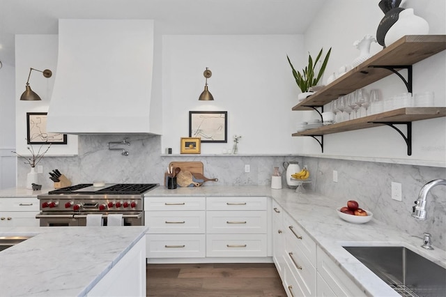 kitchen with range with two ovens, open shelves, white cabinetry, a sink, and light stone countertops