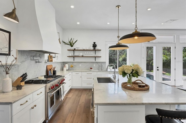 kitchen featuring range with two ovens, light stone counters, a sink, white cabinets, and open shelves