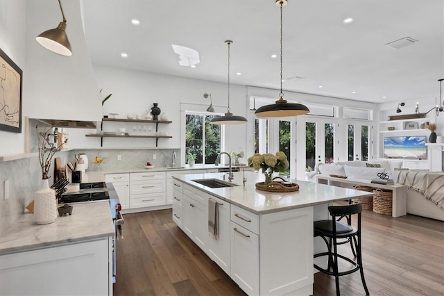 kitchen featuring pendant lighting, open shelves, white cabinets, a sink, and an island with sink