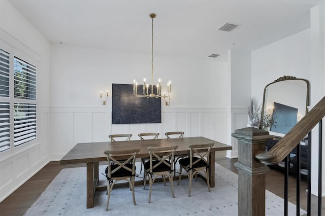 dining room featuring a notable chandelier, visible vents, a decorative wall, and wood finished floors