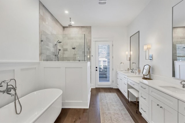 bathroom with a decorative wall, a freestanding bath, a shower stall, vanity, and wood finished floors