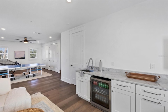 kitchen featuring beverage cooler, light stone counters, white cabinets, and a sink