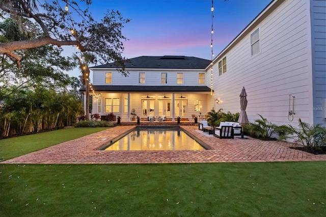 rear view of house featuring ceiling fan, a patio, a lawn, and an outdoor pool