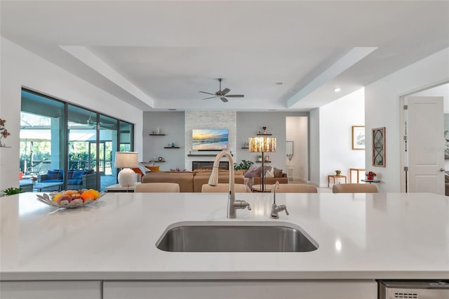 kitchen featuring sink, a large fireplace, a raised ceiling, and ceiling fan