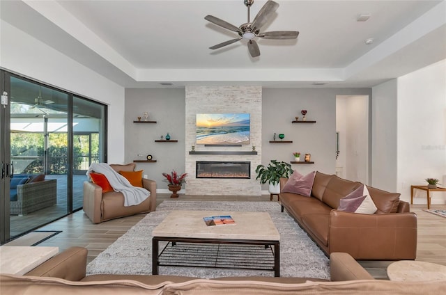 living room with a raised ceiling, ceiling fan, a large fireplace, and light wood-type flooring