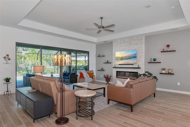 living room with ceiling fan, a fireplace, and a tray ceiling