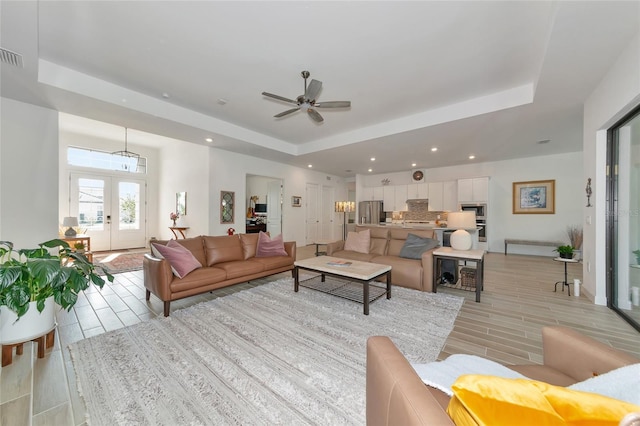 living room with a tray ceiling, french doors, and ceiling fan