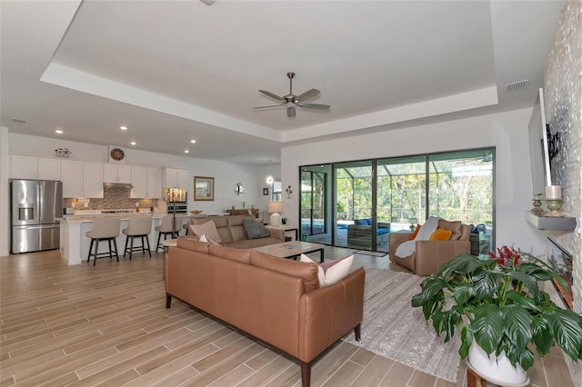 living room featuring ceiling fan and a raised ceiling