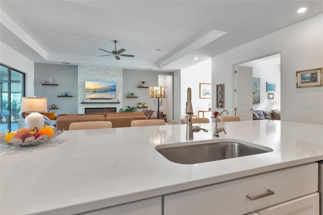 kitchen with a fireplace, a raised ceiling, sink, and white cabinets