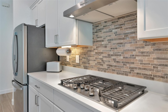 kitchen featuring tasteful backsplash, wall chimney range hood, stainless steel gas cooktop, and white cabinets