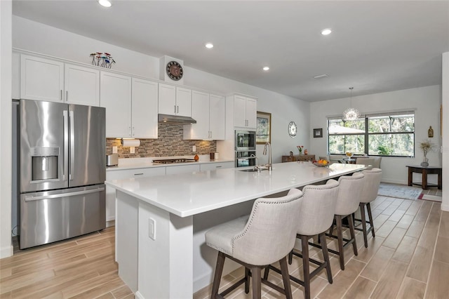 kitchen featuring stainless steel appliances, white cabinetry, tasteful backsplash, and a center island with sink