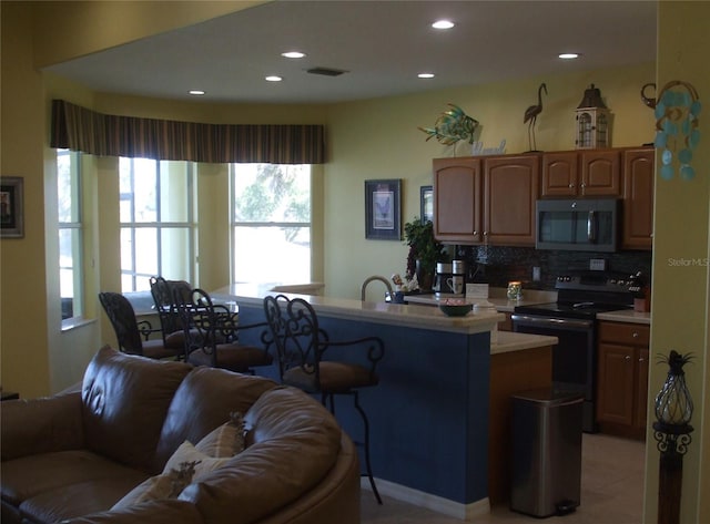 kitchen featuring tasteful backsplash, a kitchen bar, light tile patterned floors, electric range, and kitchen peninsula