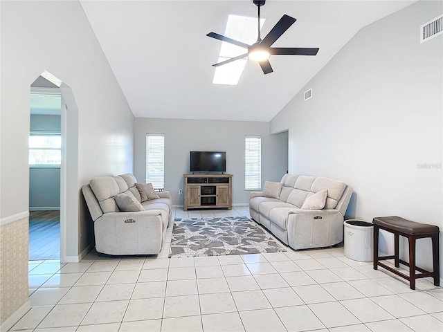 living room with ceiling fan, a skylight, high vaulted ceiling, and light tile patterned floors