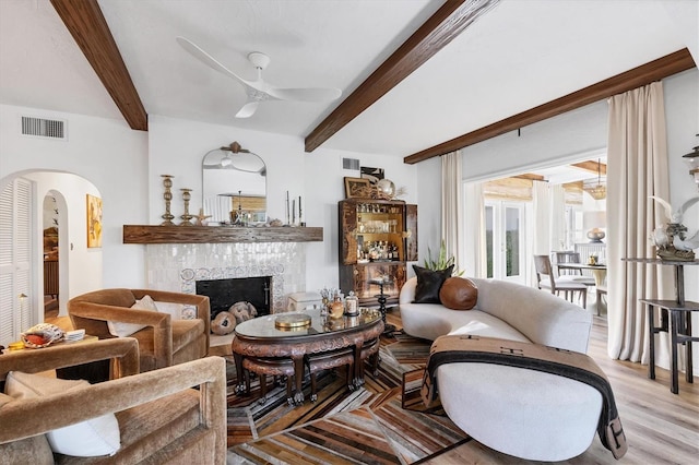 living room with a tiled fireplace, beam ceiling, light hardwood / wood-style flooring, and ceiling fan