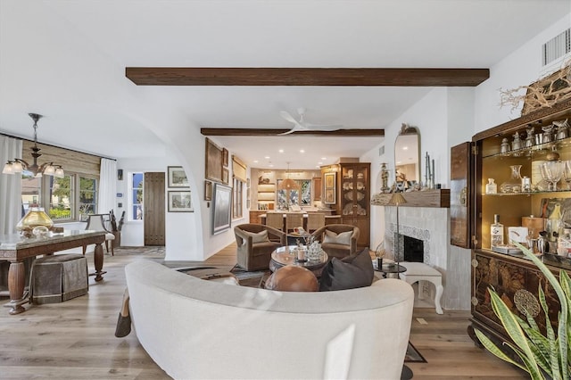 living room with beamed ceiling, ceiling fan with notable chandelier, a fireplace, and light hardwood / wood-style flooring