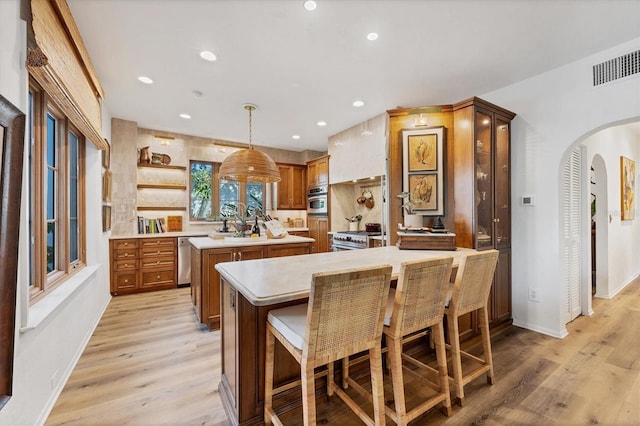 kitchen with appliances with stainless steel finishes, a center island, light hardwood / wood-style flooring, and decorative light fixtures