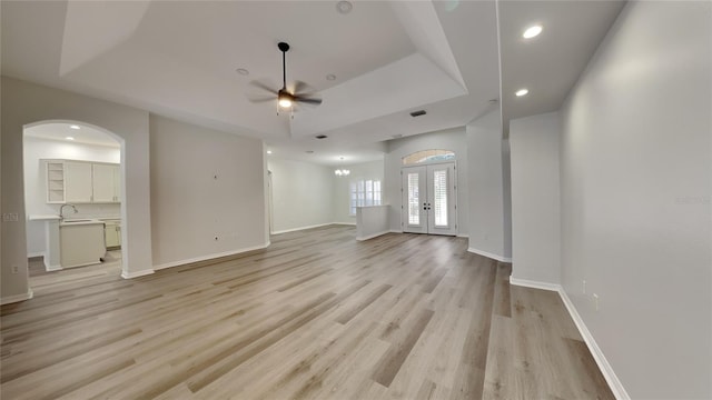 unfurnished living room with french doors, sink, light hardwood / wood-style flooring, a tray ceiling, and ceiling fan