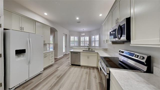 kitchen featuring sink, stainless steel appliances, light hardwood / wood-style floors, decorative light fixtures, and kitchen peninsula