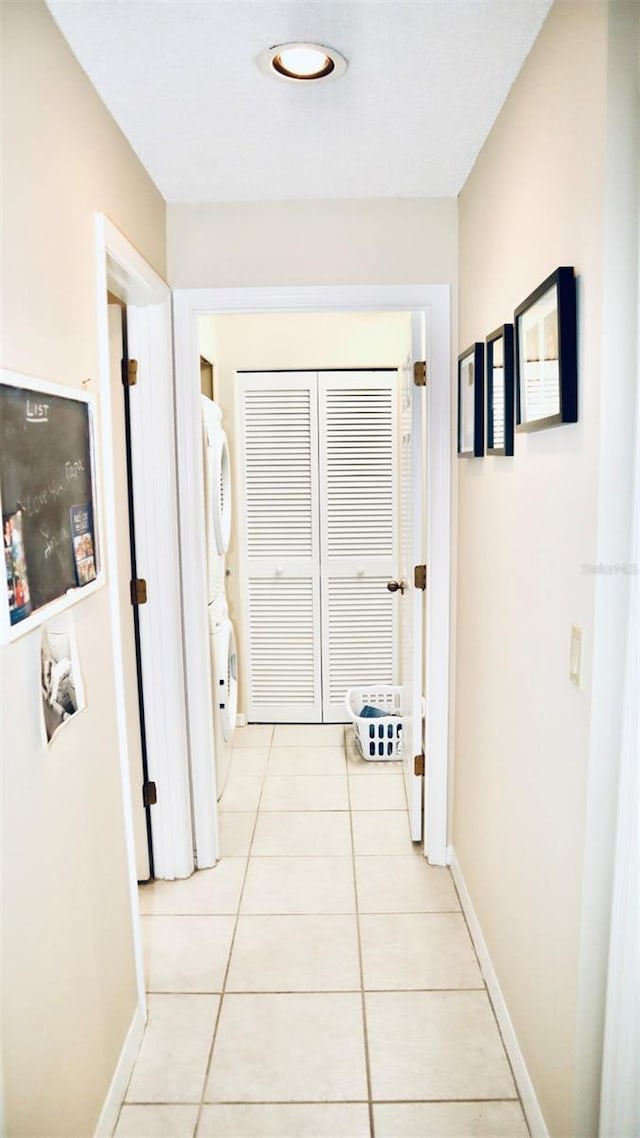 hall featuring stacked washer and clothes dryer and light tile patterned flooring