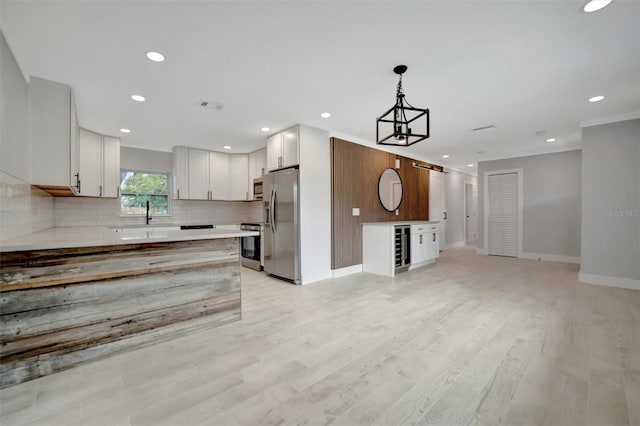 kitchen with appliances with stainless steel finishes, pendant lighting, white cabinetry, decorative backsplash, and light hardwood / wood-style floors