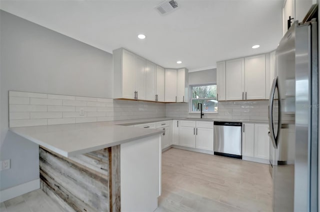 kitchen with white cabinetry, sink, decorative backsplash, kitchen peninsula, and stainless steel appliances