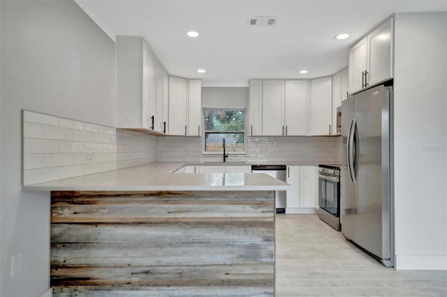 kitchen with light hardwood / wood-style flooring, backsplash, stainless steel appliances, white cabinets, and kitchen peninsula