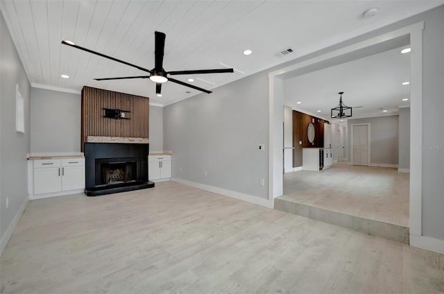 unfurnished living room with a large fireplace, ceiling fan, wood ceiling, crown molding, and light wood-type flooring