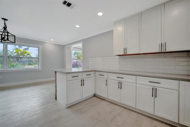 kitchen featuring tasteful backsplash, white cabinets, hanging light fixtures, kitchen peninsula, and light hardwood / wood-style flooring